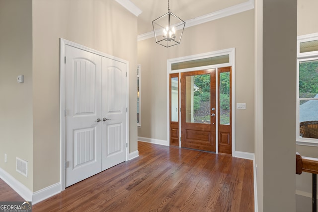 entrance foyer featuring dark wood-type flooring, crown molding, and an inviting chandelier