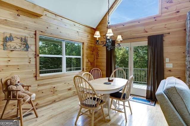 dining space featuring light wood-type flooring, lofted ceiling, a healthy amount of sunlight, and wooden walls