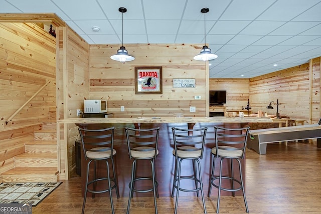 bar with pendant lighting, wood walls, a drop ceiling, and dark hardwood / wood-style flooring