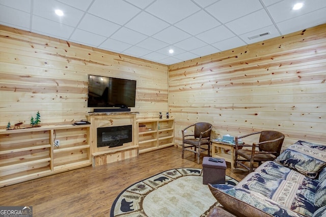 living room with hardwood / wood-style flooring, wooden walls, and a drop ceiling