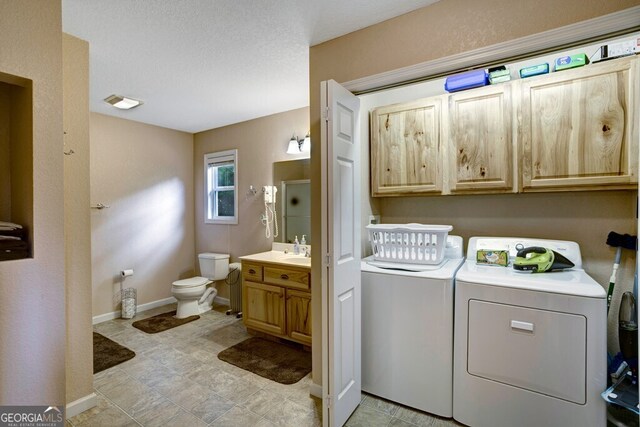 clothes washing area with cabinets, a textured ceiling, sink, and washing machine and clothes dryer