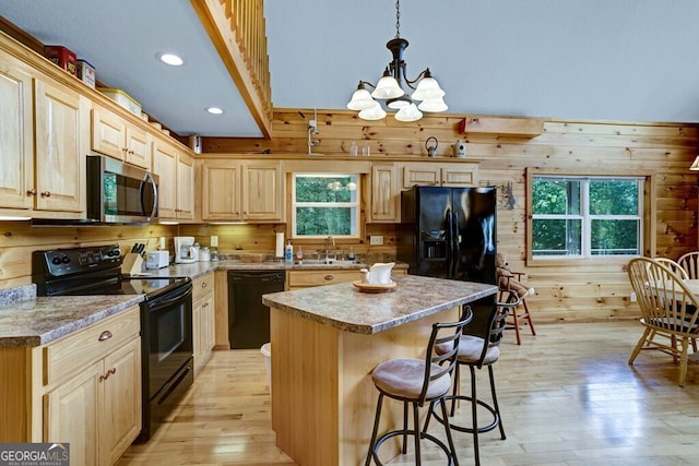 kitchen featuring hanging light fixtures, black appliances, light hardwood / wood-style floors, and wood walls