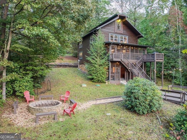 back of property featuring a deck, a yard, a sunroom, and a fire pit