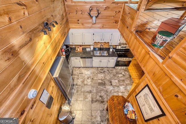 kitchen with appliances with stainless steel finishes, wood walls, white cabinetry, and sink