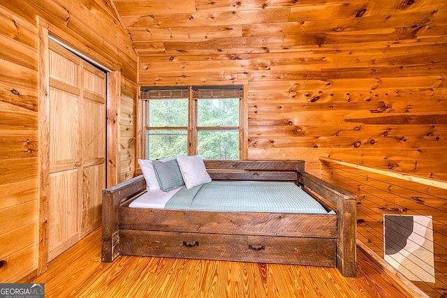 bedroom with vaulted ceiling, a closet, wood walls, and light hardwood / wood-style floors