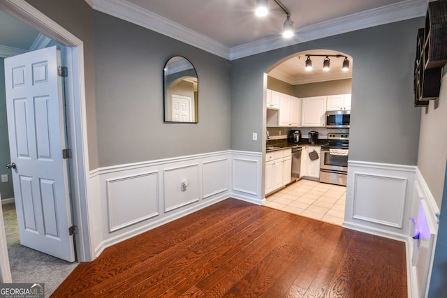 kitchen featuring rail lighting, white cabinets, stainless steel appliances, light hardwood / wood-style flooring, and ornamental molding