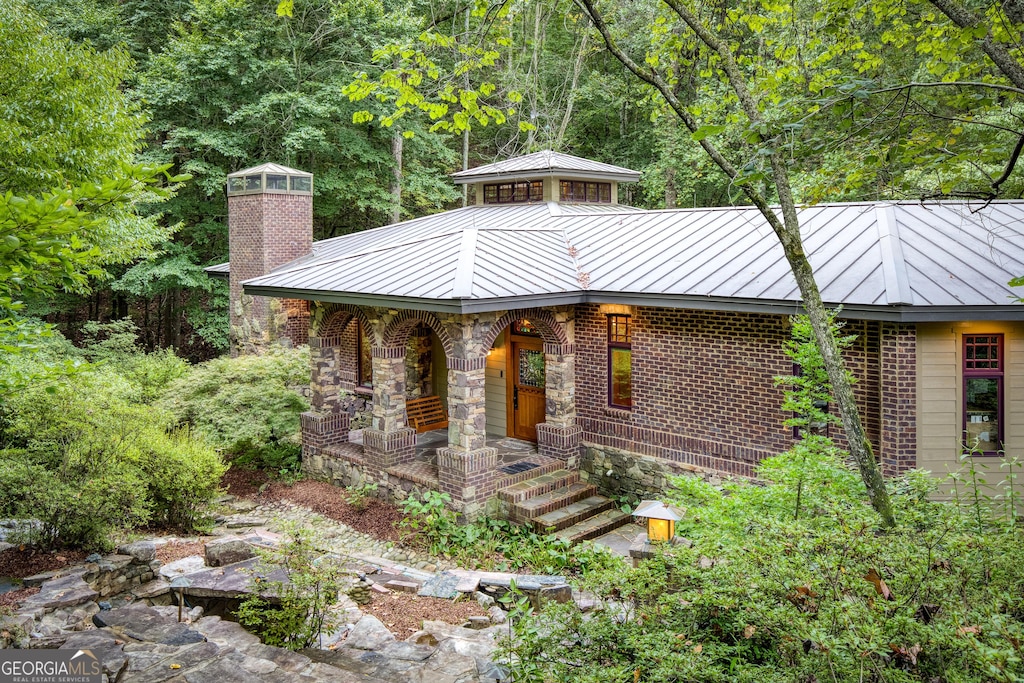 view of front of home with brick siding, a chimney, a porch, a standing seam roof, and metal roof