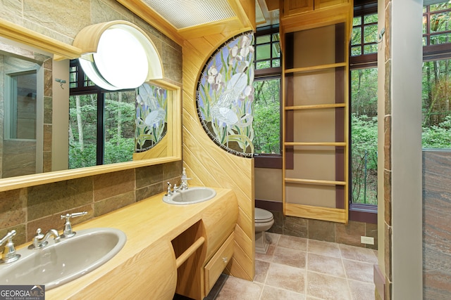 bathroom featuring vanity, wood walls, tile patterned flooring, backsplash, and toilet