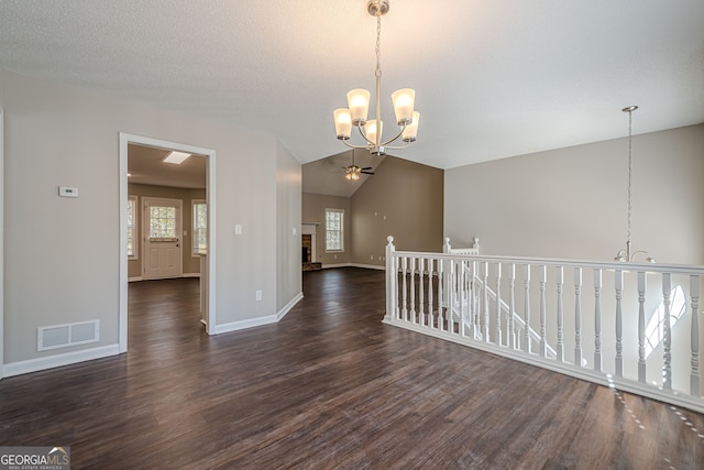 empty room with a textured ceiling, vaulted ceiling with skylight, dark wood-type flooring, and ceiling fan with notable chandelier