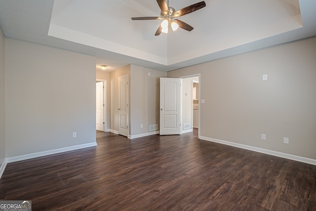 unfurnished room with a tray ceiling, ceiling fan, and dark hardwood / wood-style flooring