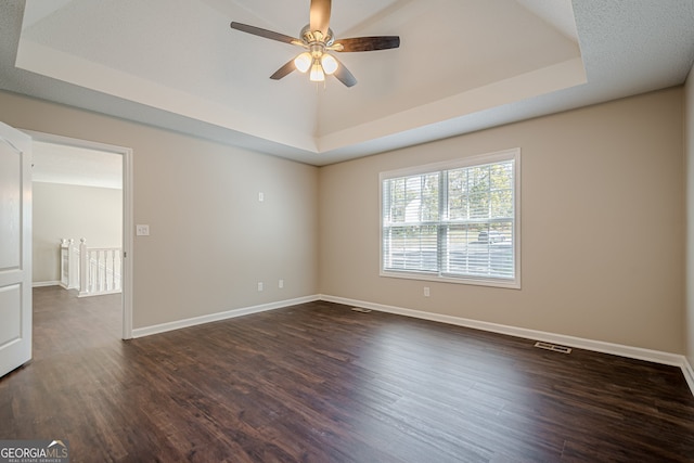 spare room featuring dark hardwood / wood-style flooring, a raised ceiling, and ceiling fan