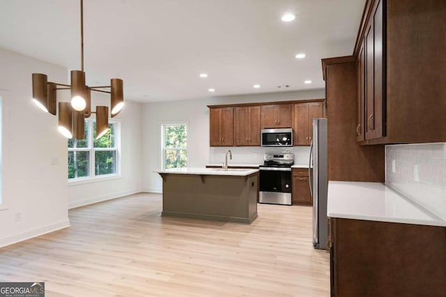 kitchen featuring appliances with stainless steel finishes, light hardwood / wood-style floors, sink, and an island with sink