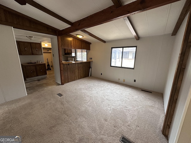 unfurnished living room with light colored carpet, wooden walls, and lofted ceiling with beams