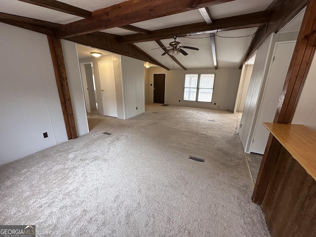 unfurnished living room with wooden walls, carpet flooring, vaulted ceiling with beams, and ceiling fan