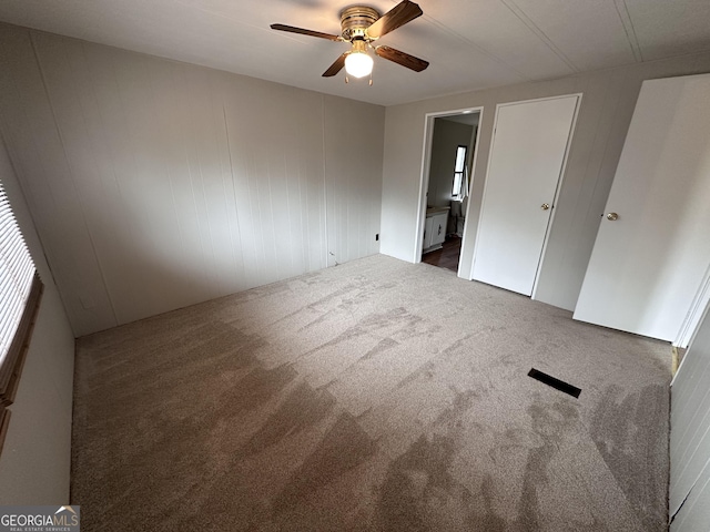 unfurnished bedroom featuring connected bathroom, dark carpet, and ceiling fan