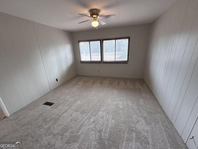 spare room featuring ceiling fan, wooden walls, and carpet floors