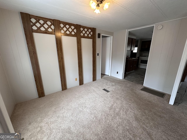 unfurnished bedroom with wood walls, ensuite bath, and dark colored carpet