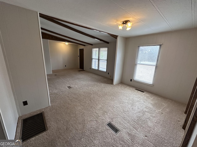 empty room featuring beam ceiling, carpet, and a textured ceiling