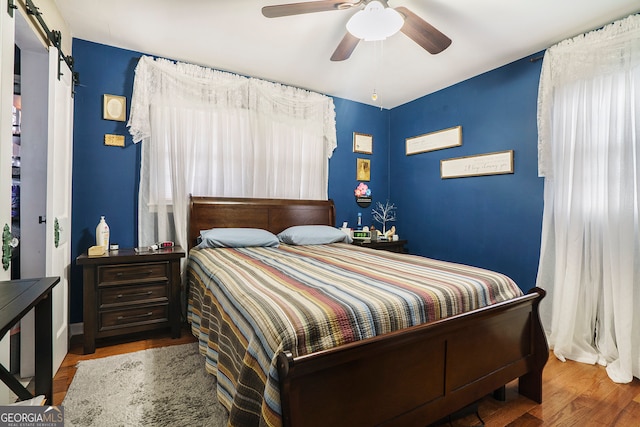 bedroom featuring a barn door, hardwood / wood-style floors, and ceiling fan