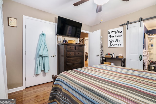 bedroom with ceiling fan, light hardwood / wood-style floors, and a barn door