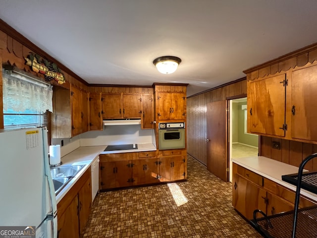 kitchen with crown molding, white appliances, wooden walls, and sink