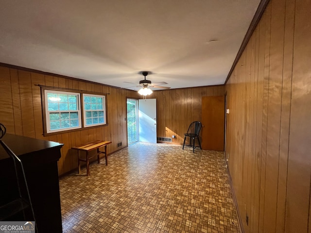 interior space with ornamental molding, wooden walls, and ceiling fan