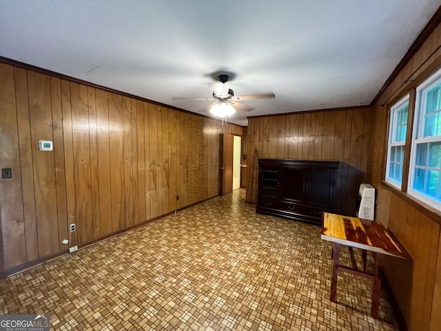 unfurnished room with ornamental molding, wood walls, and ceiling fan