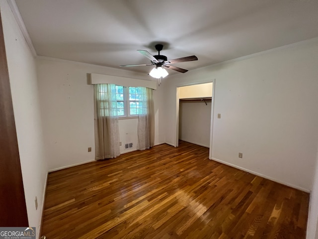 unfurnished bedroom with a closet, a spacious closet, dark hardwood / wood-style floors, ornamental molding, and ceiling fan