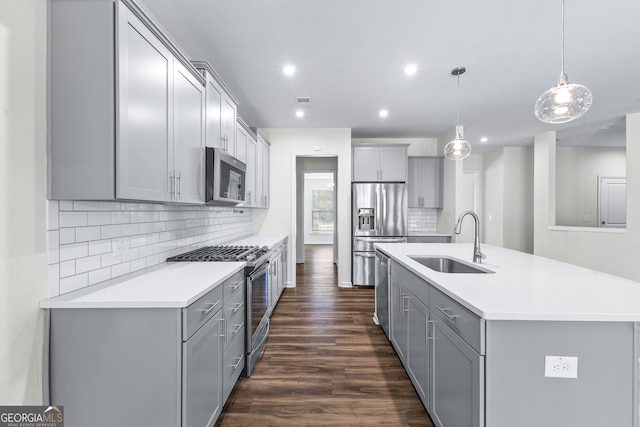 kitchen with dark hardwood / wood-style floors, an island with sink, sink, decorative light fixtures, and appliances with stainless steel finishes