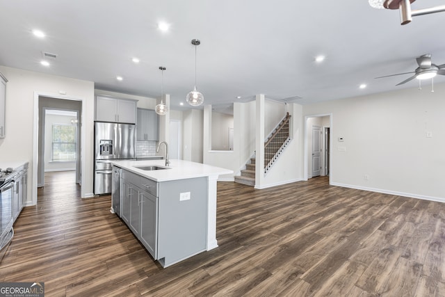 kitchen featuring stainless steel fridge, decorative light fixtures, gray cabinets, dark wood-type flooring, and a kitchen island with sink