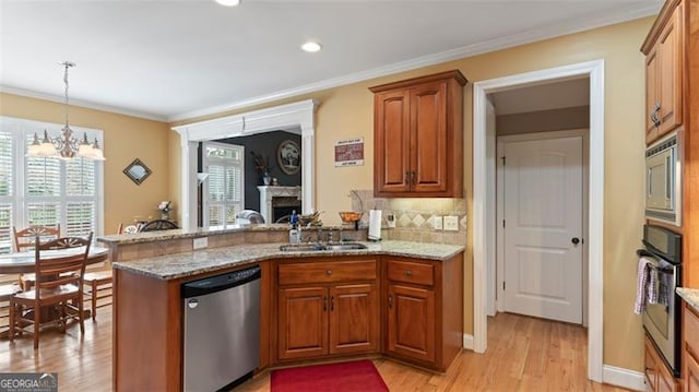 kitchen with appliances with stainless steel finishes, light hardwood / wood-style floors, kitchen peninsula, an inviting chandelier, and sink