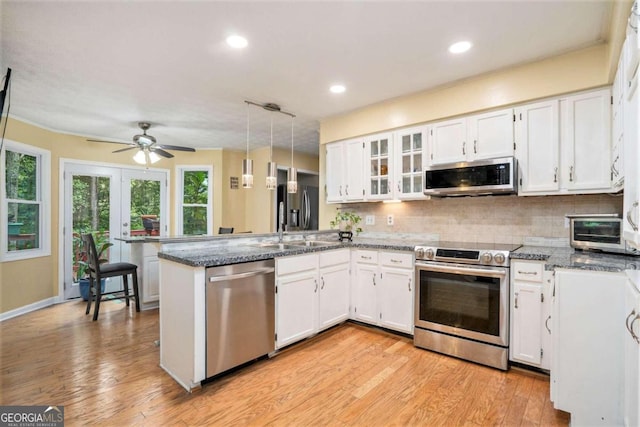 kitchen with white cabinets, hanging light fixtures, kitchen peninsula, appliances with stainless steel finishes, and light wood-type flooring