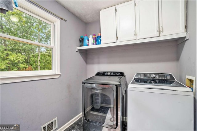 laundry room with a textured ceiling, washer and dryer, and cabinets