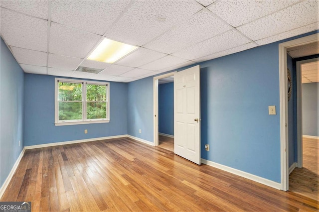 empty room with a drop ceiling and hardwood / wood-style floors