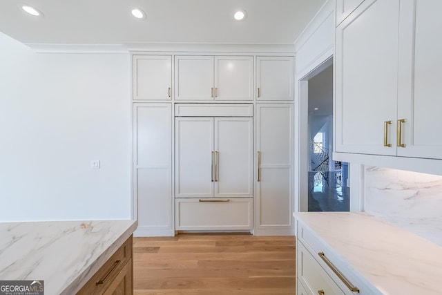 kitchen featuring white cabinets, decorative backsplash, light wood-type flooring, ornamental molding, and light stone counters