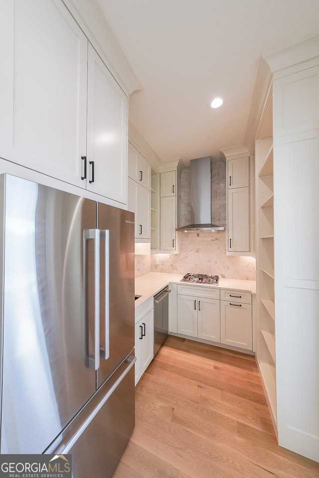 kitchen featuring white cabinets, stainless steel appliances, light hardwood / wood-style floors, and wall chimney range hood