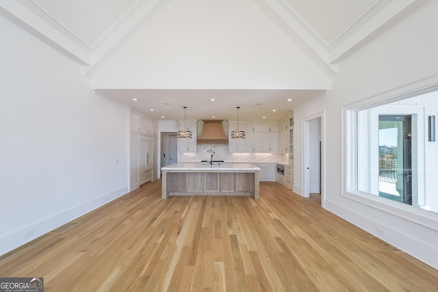 kitchen with premium range hood, sink, decorative light fixtures, light hardwood / wood-style flooring, and a large island