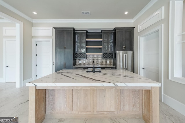 kitchen featuring light stone countertops, a large island with sink, high end fridge, and ornamental molding