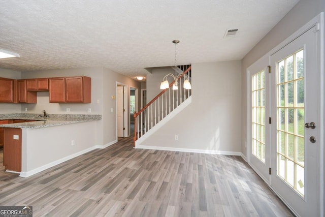 kitchen with wood-type flooring, a notable chandelier, kitchen peninsula, decorative light fixtures, and light stone countertops