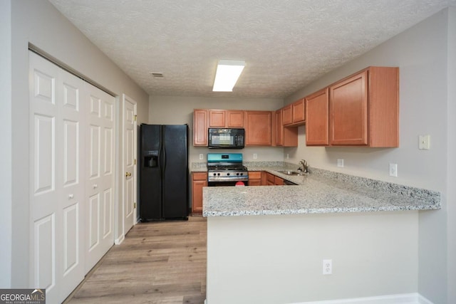 kitchen with a textured ceiling, sink, kitchen peninsula, light hardwood / wood-style flooring, and black appliances