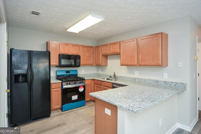 kitchen with light wood-type flooring, sink, kitchen peninsula, black appliances, and light stone countertops