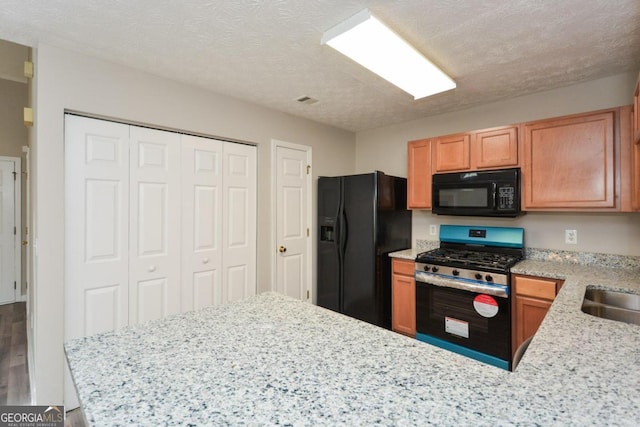 kitchen featuring a textured ceiling, black appliances, kitchen peninsula, and light stone counters