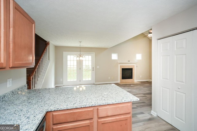 kitchen with light stone counters, kitchen peninsula, a textured ceiling, light hardwood / wood-style flooring, and decorative light fixtures