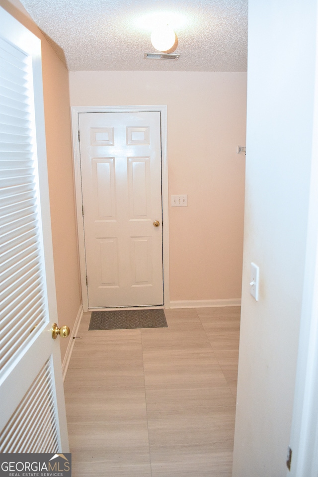 corridor with light hardwood / wood-style flooring and a textured ceiling