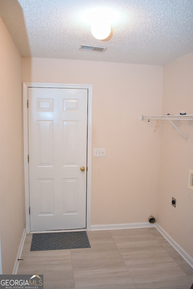 laundry room featuring a textured ceiling, light hardwood / wood-style flooring, and electric dryer hookup