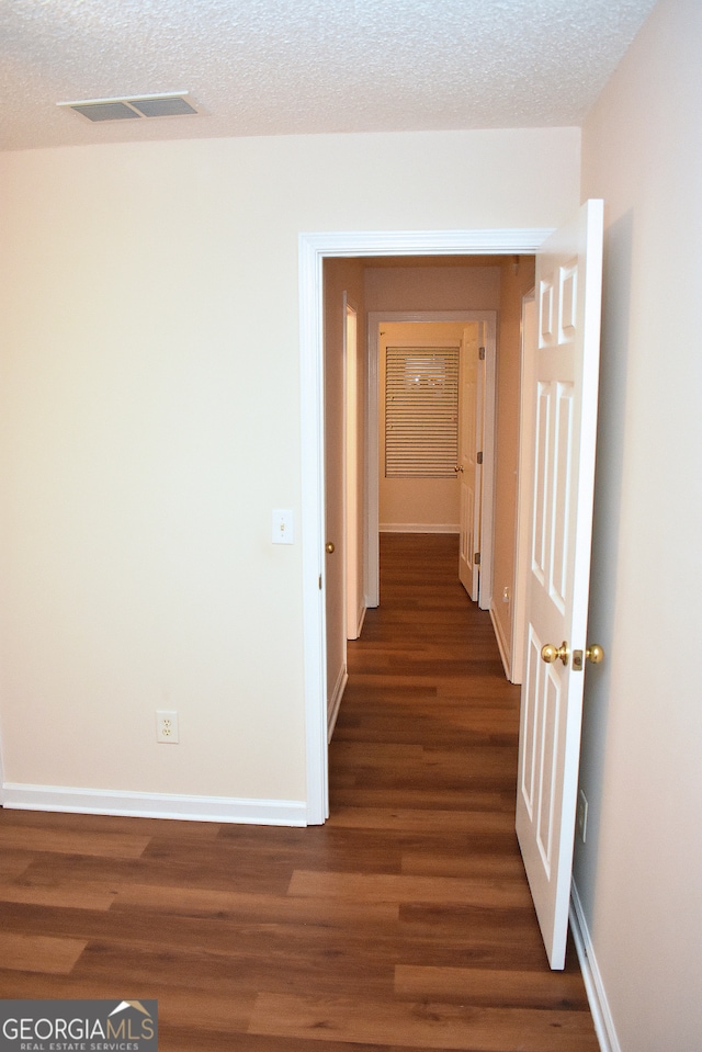 corridor with a textured ceiling and dark hardwood / wood-style flooring