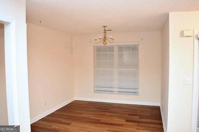 spare room featuring dark wood-type flooring, a notable chandelier, and a textured ceiling