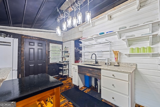 kitchen with sink, white fridge, white cabinetry, and wood walls