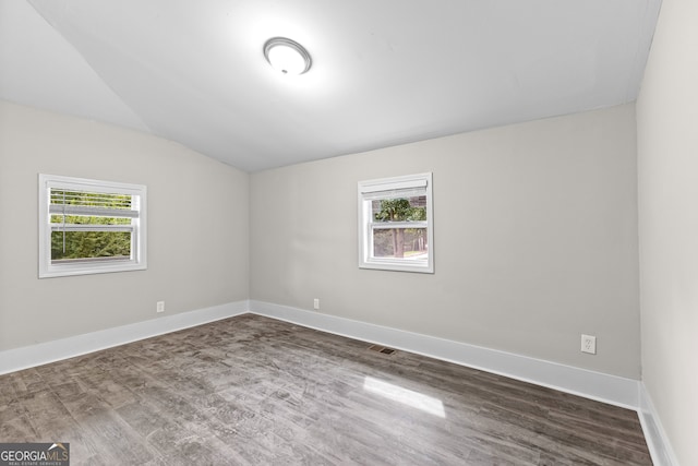 empty room with a healthy amount of sunlight, vaulted ceiling, and dark hardwood / wood-style flooring