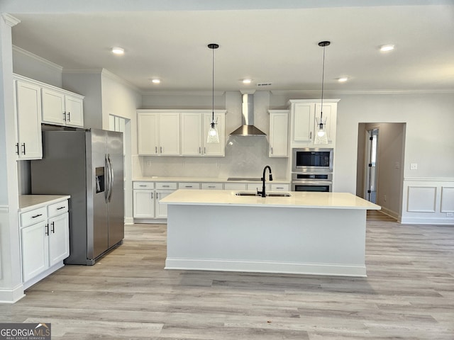 kitchen with decorative light fixtures, white cabinetry, a kitchen island with sink, appliances with stainless steel finishes, and wall chimney exhaust hood